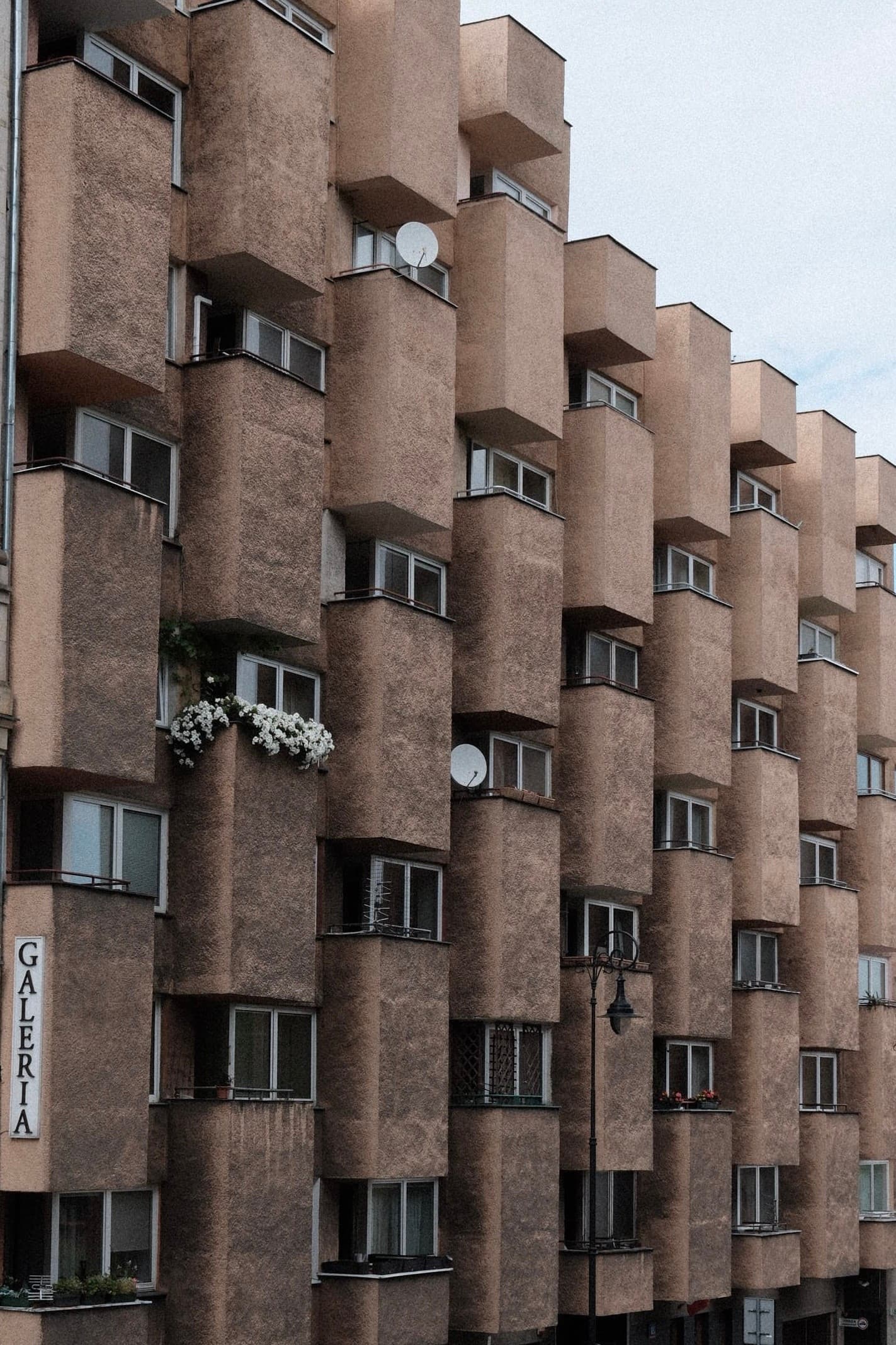 Multi story brick apartment building with repeating protruding balconies and small windows under an overcast sky